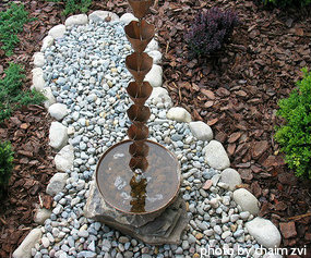 Copper rain chain hanging into copper hammered basin filled with water on rock bed, decorative rain chains, unique rain chains,chains decorative, decorative rain, hot Mediterranean, hammered basin, copper hammered, gardening joy, outdoor gardening.