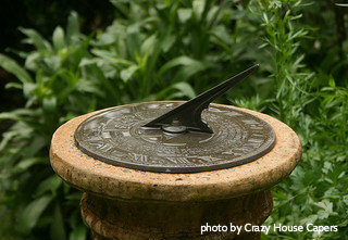 Metal sundial mounted on top of stone decorative column pedestal in garden, metal sundials, decorative backyard accent.
