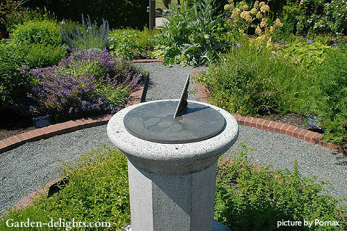 Sundial mounted on top of stone pedestal with garden walkway surrounding with plants,stone column sundials,garden timepieces.