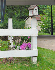 White wood birdhouse with red roof mounted on wooden fence post, decorative white birdhouses, unique birdhouses.