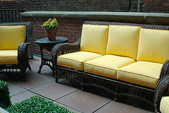 Wholesale Outdoor Furniture, Wicker outdoor couch with two chairs with yellow cushions and patio table with yellow flowers on top of table.