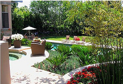 Tropical Outdoor Furniture, two Wicker chairs and three lounge chairs surrounded by tropical plants and decorative pools.