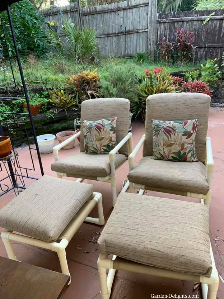 Two single patio furniture chairs with matching footstool with gray furniture cushions and floured pillows, exterior grade PVC, plastic outdoor furniture.