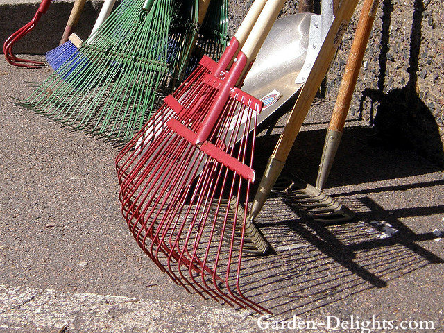 Metal garden rakes both red and green standing up against a wall, types of garden tools, essential gardening tools,basic gardening tools.